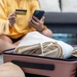 A woman planning a trip using credit card and phone while preparing a suitcase.