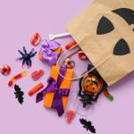 Halloween shopping bag with candies and gifts on a lilac background.