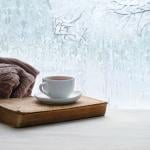 A cup of coffee on a home window showing peak winter season.