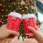 Holiday coffee cups are cheered in front of a Christmas tree.