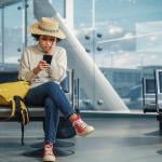 A woman in an airport is checking flight updates in phone while looking worried.