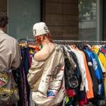 Two people browsing through vintage jackets at a thrift stand.