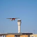 A single engine plane soaring near an airport control tower.