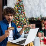 A guy looking confused at his credit card while online shopping for the holidays.