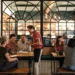 A waiter taking orders from customers in a busy restaurant.