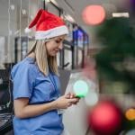 Medical professional in blue scrubs and a Santa hat texting in a holiday setting on break.