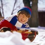 Smiling child sledding in the winter in the 1960s or '70s.