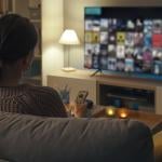 A woman relaxing at home is browsing through her smart TV looking for something to watch.