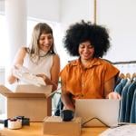 Two women who are owners of a clothing small business happily looking at orders from a laptop.