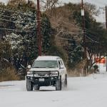 A white 4x4 truck braving thick snow on a Texas road after a blizzard.