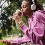 A woman taking a break from working out by drinking coffee while listening to music in the park.