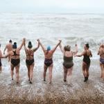 A group of nine adults happily going for a swim at the beach.