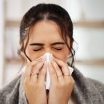 Sick person with COVID sneezing into tissue.