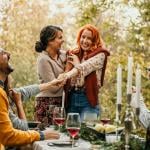 A lesbian couple showing off an engagement ring and celebrating a happy engagement with their friends.