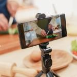 A male food influencer vlogging his cooking session at home using a phone on a tripod.