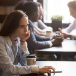 Young woman sits by herself at a coffee shop with drink in front of her.