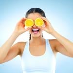 A woman holds orange slices over her eyes.