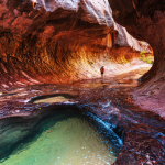 Hiker wading through the waters of the Narrows slot canyon in Zion National Park, Utah.