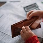 A woman's hands opening her empty wallet over a pile of power bills.