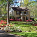 A country home with a large front yard surrounded by shaded trees and spring blooms