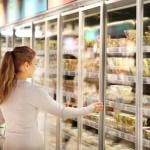 A young woman shopping in the frozen foods section of a supermarket.