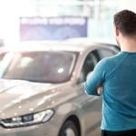 A pensive man looking at a car in a dealership.