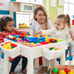 Kindergarten teacher sitting with two children playing with construction blocks in a classroom