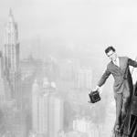 Photographer Jack Reilly precariously perched from the 72nd story of the world's tallest building, the Bank of Manhattan structure, in progress of construction in Wall Street, New York City in 1929. A panorama of New York's prominent business section is seen in the background, with the Woolworth building, in the upper left.