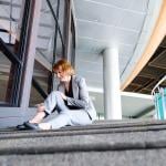 A woman at work sitting in pain after falling down the workplace stairs.