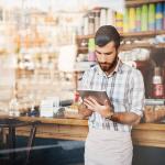 A coffee shop owner using his tablet by the counter.