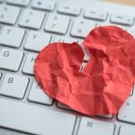 A red broken heart made out of paper on top of a computer keyboard depicting online dating scams.