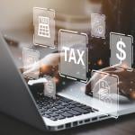 Businessperson using a laptop and holographic concepts of tax are illustrated.