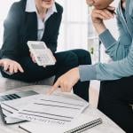 Insurance advisor holding up a calculator while the insurance policy owner reviews documents.