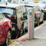 A lane of electric cars being charged on the side of a street.