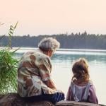 Grandparent sits with grandchild, overlooking the river on a warm day.