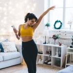 Cheerful young woman dancing to music she is listening to while on a workout at home.