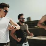 Three men on a fitness run and one of them is looking at his smartwatch for tracking.