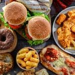 Trays of fast food such as donuts, burgers, chicken nuggets, fries and pizza.