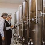 Two winemaking professionals inspecting the large winery storage and equipment.