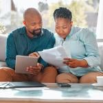 A middle aged black couple reviewing forms and looking up information at home using a tablet.