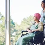 A woman in her 30s pushes another older woman in a wheelchair down a hallway.