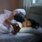 Young woman lying on her bed at home scrolling on social media.