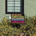 "We believe" yard sign that says, "Science is real, womens rights are human rights, black lives matter, no human is illegal, love is love, diversity makes us stronger” outside of a green home.