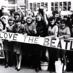Screaming Beatles fans holding banners and waving at the band, circa 1964