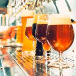 Different types of beer in unique glasses with bartender in background.