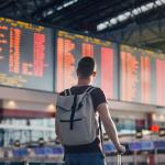 A man with a backpack looking at a departure and arrival schedule board in an airport.