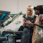 A shirt printing business and its workers looking at information in a phone.