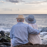 Elderly couple sitting on a rocky beach and looking at the horizon