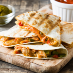 Mexican quesadilla with chicken, cheese and peppers on a wooden table.