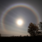 A lunar rainbow and a shining full moon against a clear, dark sky
